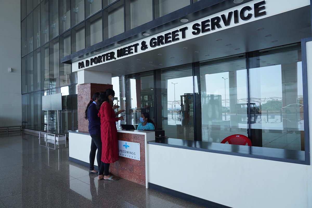 Two people interacting at Kannur Airport's reception desk, possibly inquiring about services or checking in at a venue.